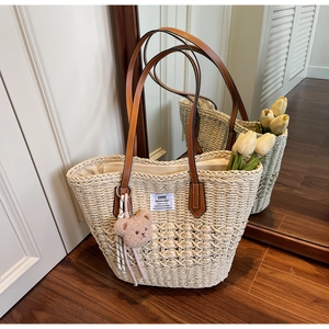 Dettaglio della borsa tote in paglia intrecciata con spalline in pelle marrone e ciondolo