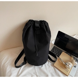 Detail of black nylon drawstring bucket bag with metal hardware on casual bedding
