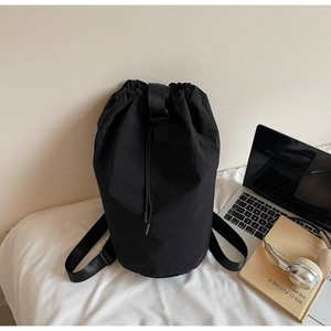Detail of minimalist black nylon drawstring bucket bag with adjustable strap and laptop on a bed