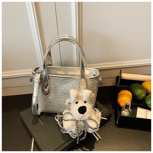 Detail of silver sequin handbag with wave texture and plush bear charm on green book