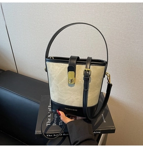 Detail of canvas bucket bag with black leather trim and golden metal snap closure