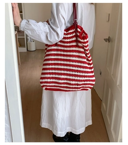 Close-up of red and white striped knit tote bag with deep red leather strap on a model