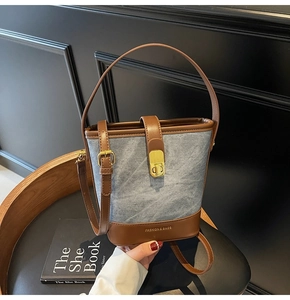 Detail of vintage denim bucket bag with brown leather trim and golden twist lock closure