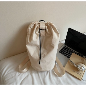Close-up of beige drawstring bucket bag on white bedding with lifestyle accessories