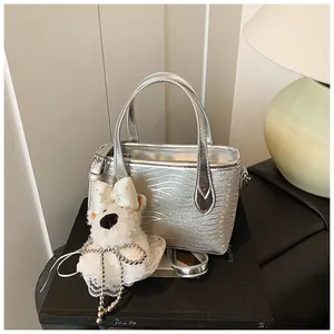 Detail of silver wavy glitter handbag featuring a cute plush dog charm with pearl chain