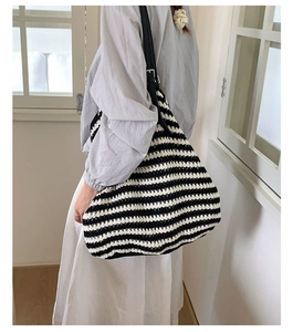 Model wearing a striped woven straw tote bag with black shoulder strap in a bright room