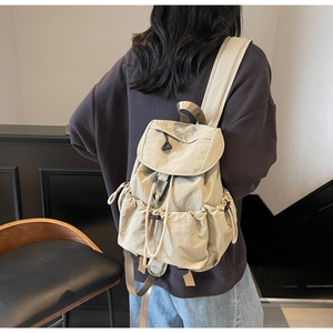 Back view of a beige drawstring nylon backpack on model showing wide shoulder straps