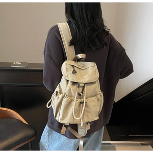Rear view of model wearing a beige canvas backpack with flap top and side drawstring pockets