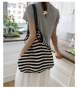 Detailed view of striped straw tote bag with black leather straps on person