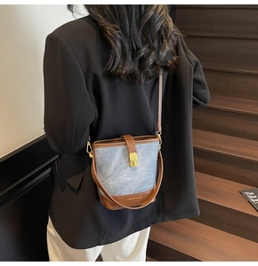 Detail of blue textured fabric bucket bag with brown leather trim and gold buckle