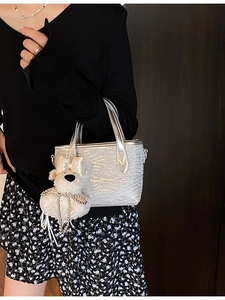 Silver glitter handbag with crackle texture and white plush bear charm on dark background