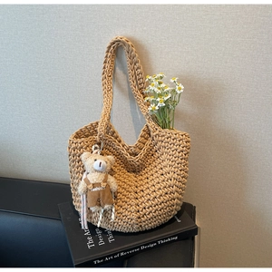 Detailed close-up of a khaki woven bucket bag with a cute teddy bear charm on books