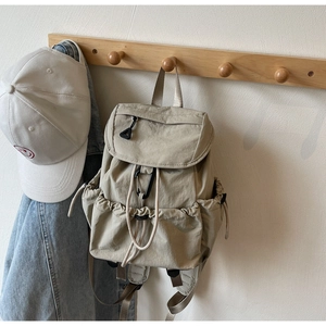 Detail view of beige nylon drawstring backpack with flap closure and black D-buckle detail