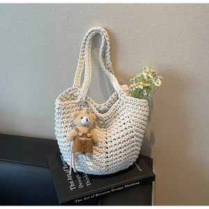 Detail of cream woven tote bag with a brown teddy bear charm on art books