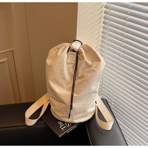 Detail of off-white drawstring bucket bag with nylon texture on a dark leather surface