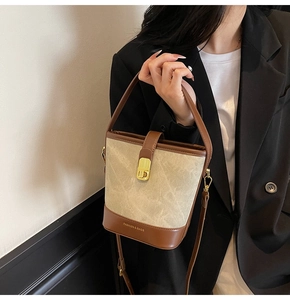 Detail of canvas bucket bag with brown leather trim and golden metal lock buckle