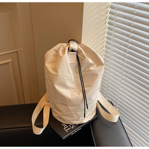 Detail of cream drawstring bucket bag showing textured nylon fabric and black cord closure