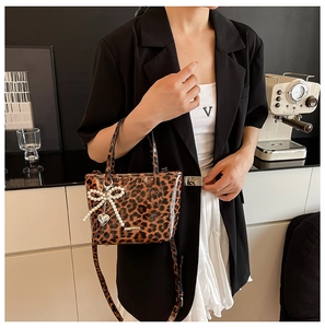 Detail of leopard print crossbody bag with glossy texture and pearl bow charm accessory