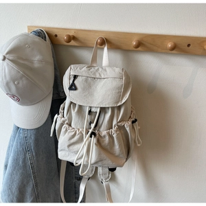 Detailed view of cream-white backpack with multiple pockets and drawstring side pockets