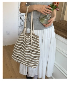 Detail of woven straw tote bag featuring khaki stripes and adjustable leather shoulder strap