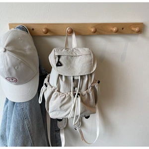 Detail showing the cream nylon backpack with drawstring side pockets and flap closure