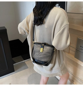 Detail of dark grey textured bucket bag with black leather trim and golden metal snap