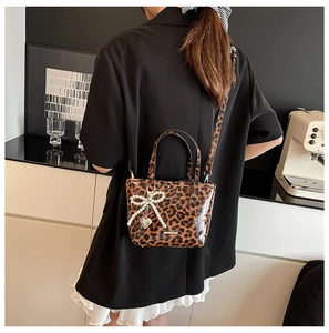 Detailed view of leopard print crossbody bag with pearl bow and heart charm on a model