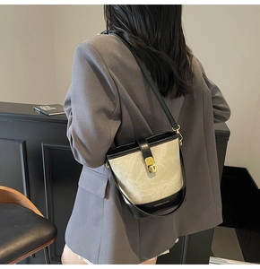 Detail of a minimalist beige and black bucket bag with a golden metal twist lock