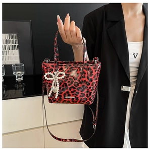 Detail of red leopard print crossbody bag with pearl bow charm and adjustable strap