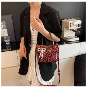 Detail of red leopard print crossbody bag with pearl bow and heart charm on a model