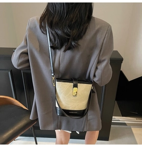 Detail of canvas bucket bag with leather trim and gold metal lock worn as crossbody