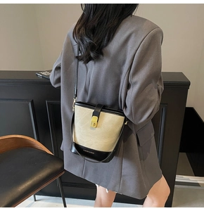Detail of two-tone bucket bag featuring beige fabric and black leather strap worn by a model
