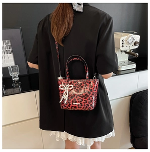 Detail of red leopard print crossbody bag with pearl bow charm and glossy finish