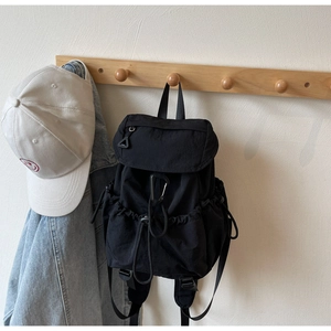 Detail of black nylon drawstring backpack and white smiley face cap on wooden coat rack
