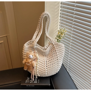 Detail of hand-knitted off-white tote bag with a cute bear plush and colorful tassel charm
