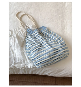 Close-up of blue and white striped crochet straw bag with a white leather shoulder strap