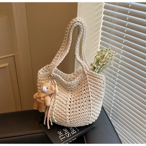 Detail of hand-woven cream tote bag with cute bear charm and tassel on a book