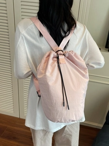 Casual light pink drawstring bucket bag with adjustable strap worn as a crossbody backpack