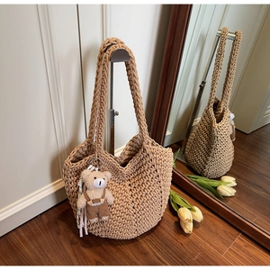 Detail of khaki woven tote bag with a small teddy bear charm on a metal display stand