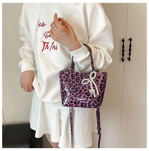 Detail of purple leopard print handbag featuring a large pearl bow charm and shoulder strap