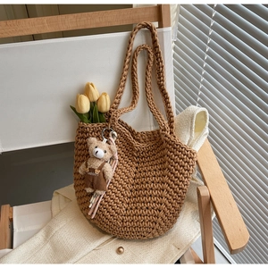 Detail of caramel woven tote bag with a cute teddy bear charm on a wooden chair