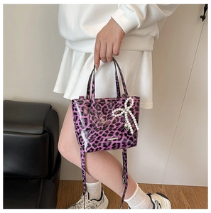 Detail of purple leopard print patent leather bag with a pearl bow charm and shoulder strap