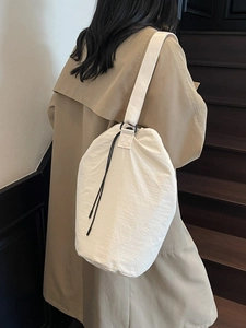 Minimalist white drawstring bucket bag with black strap on a model by wooden stairs
