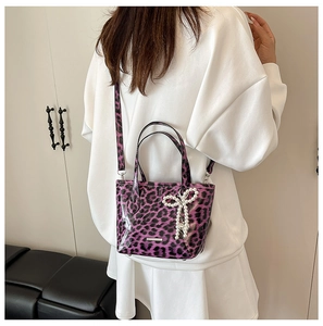 Purple leopard print mini crossbody bag with pearl bow charm shown in a lifestyle scene