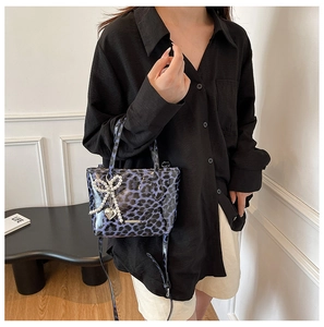 Detail of blue leopard print crossbody bag with pearl bow and heart charm on handle