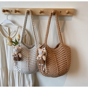 Detail of hand-woven crochet shoulder bags in cream and tan with teddy bear pendants