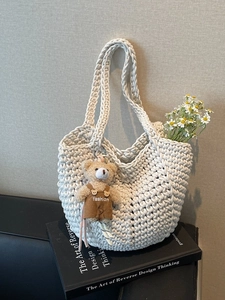 White woven crochet tote bag with a brown plush bear charm and fresh daisies inside