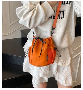 Detail view of the orange drawstring bucket bag with side mesh pocket and nylon texture