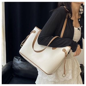 Close-up of a large beige tote bag with brown leather handles worn over the shoulder