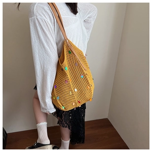 Detail of yellow knit shoulder bag with sequins and leather straps worn by a model